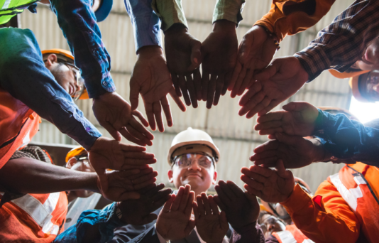 Workers standing in a circle with their hands in the middle.