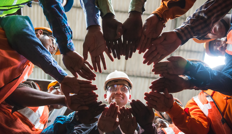 Workers standing in a circle with their hands in the middle.