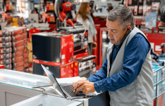 Business manager working at a hardware store and making a call while using a computer.