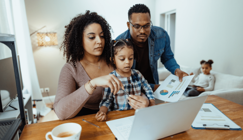 Serious multiracial family with two daughters at home. Mother working on laptop and discussing finances with husband.