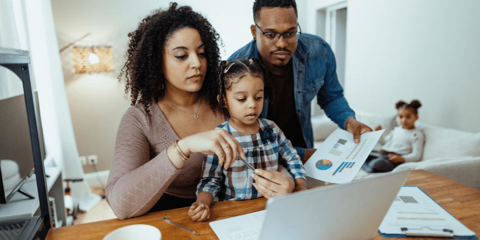 Serious multiracial family with two daughters at home. Mother working on laptop and discussing finances with husband.