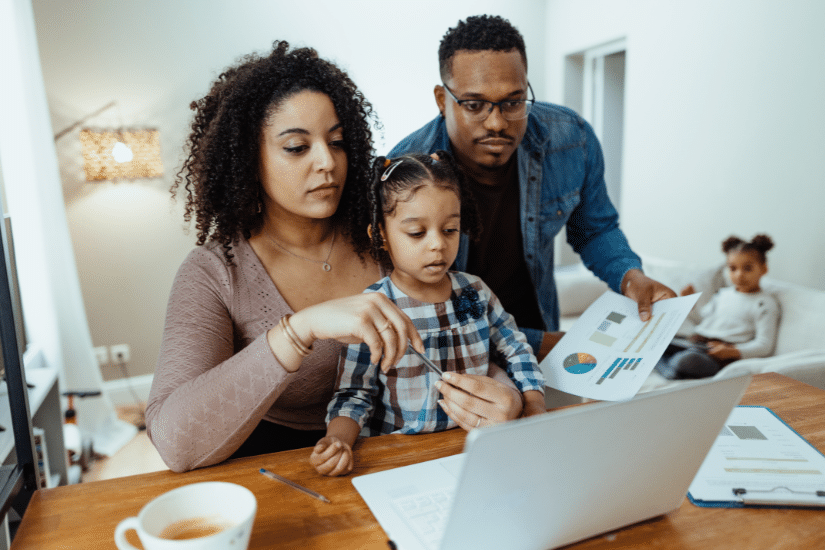 Serious multiracial family with two daughters at home. Mother working on laptop and discussing finances with husband.