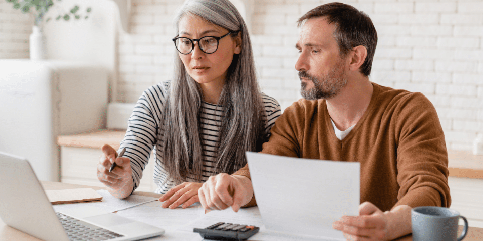 Mature middle-aged couple family wife and husband counting funds, savings declarations, investments, paperwork, financial documents, bankruptcy, court case, bills, pension with laptop.