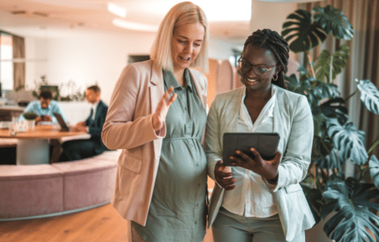 A pregnant employee and her colleague looking at an iPad.