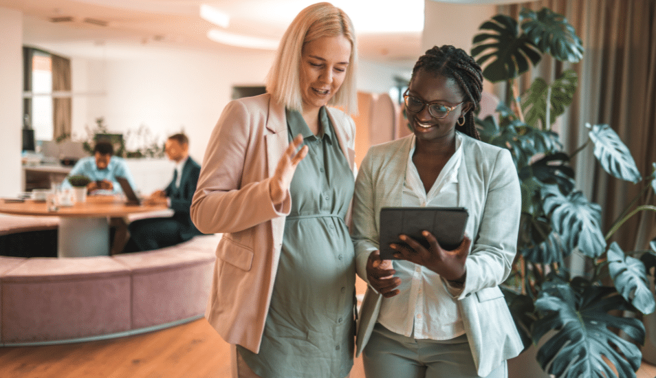 A pregnant employee and her colleague looking at an iPad.