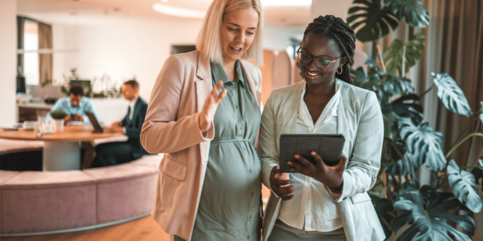 A pregnant employee and her colleague looking at an iPad.