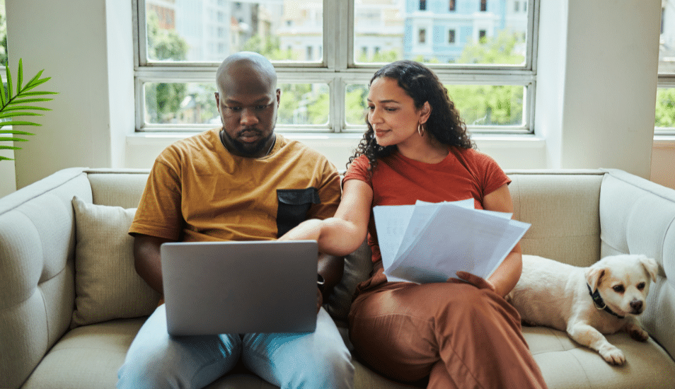 A young couple working on their budget and finances on a sofa from home with their dog using a laptop computer