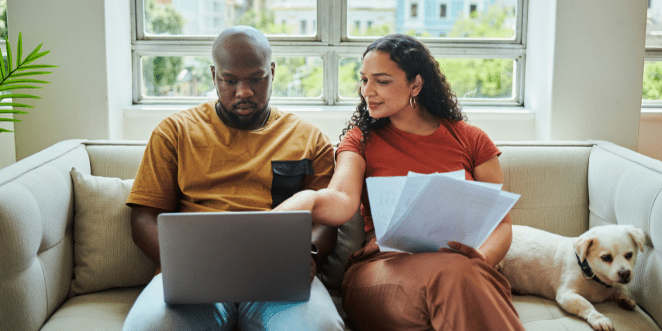 A young couple working on their budget and finances on a sofa from home with their dog using a laptop computer