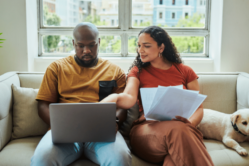 A young couple working on their budget and finances on a sofa from home with their dog using a laptop computer