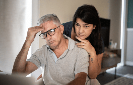 An older couple couple looking anxious while reading a computer screen