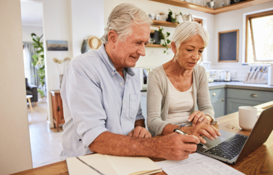 Senior couple going over their home finances together using a laptop while sitting at a table in their kitchen at home.