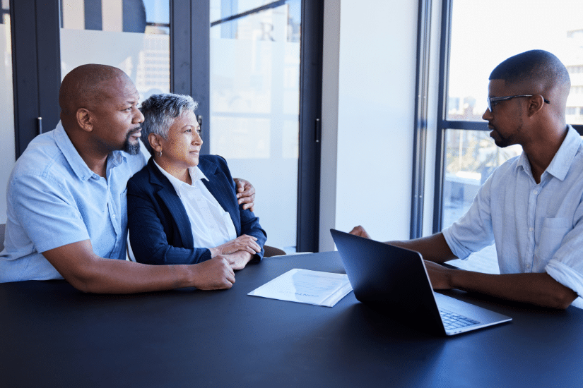 Couple going over documents with their financial advisor during a meeting together at table in his office.