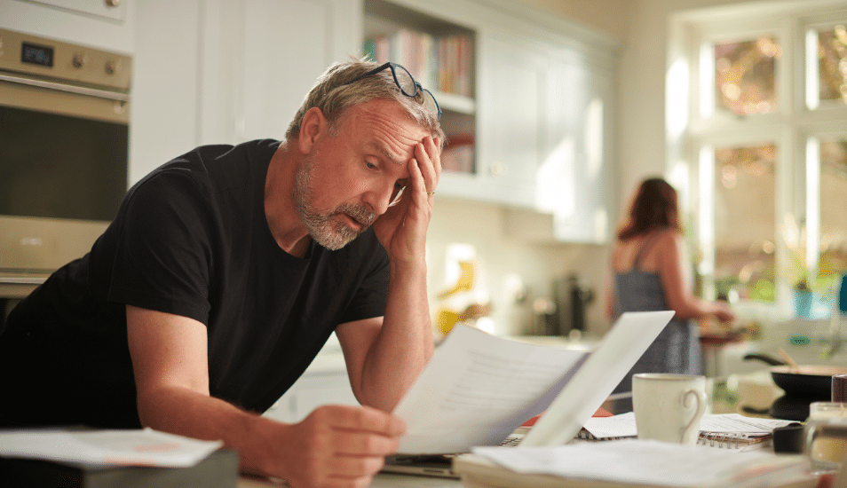 Man at kitchen counter stressed looking at bills.