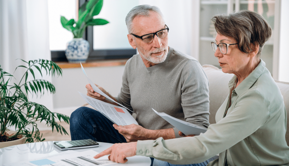 Mature couple sit on couch, calculate expenses and planning monthly budget, at home. serious husband and wife filing tax application in living room.