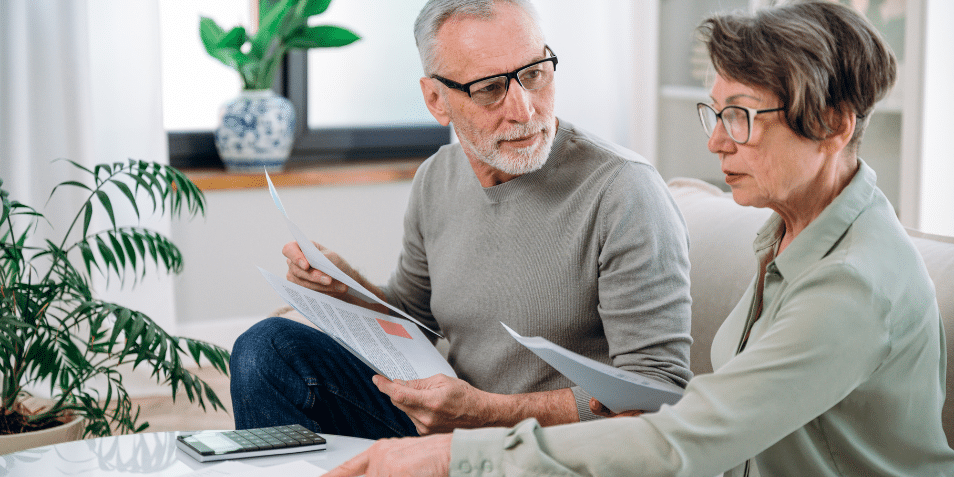 Mature couple sit on couch, calculate expenses and planning monthly budget, at home. serious husband and wife filing tax application in living room.