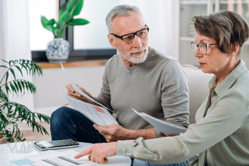 Mature couple sit on couch, calculate expenses and planning monthly budget, at home. serious husband and wife filing tax application in living room.