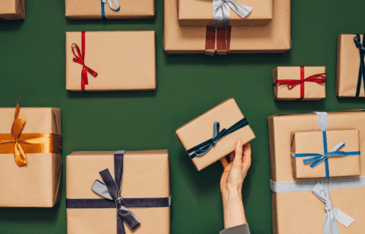 Many nicely wrapped gifts with different colored ribbons Hands of an anonymous person are putting one gift on the table.