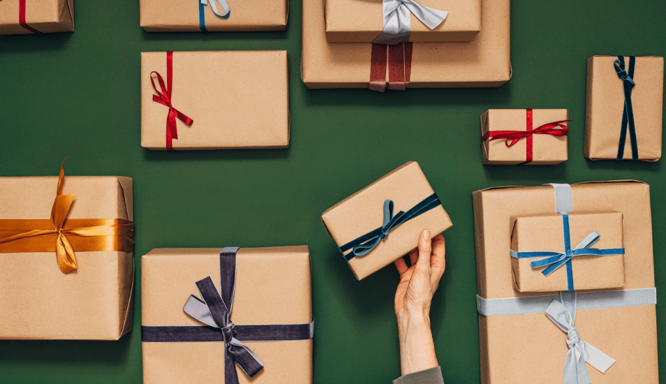 Many nicely wrapped gifts with different colored ribbons Hands of an anonymous person are putting one gift on the table.
