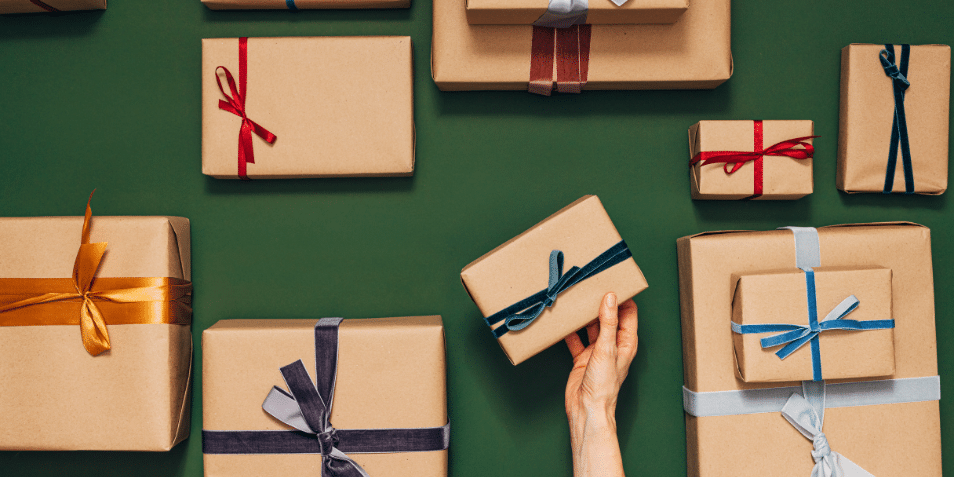 Many nicely wrapped gifts with different colored ribbons Hands of an anonymous person are putting one gift on the table.