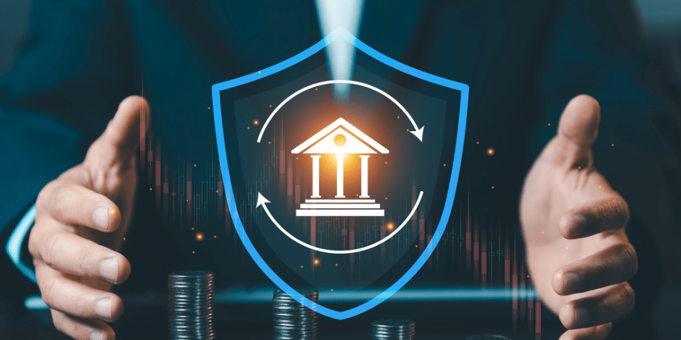 Businessman protecting bank icon inside blue shield with stacks of coins, financial insurance and capital protection concept against market volatility.