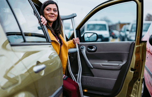 A woman on crutches stepping out of her car.
