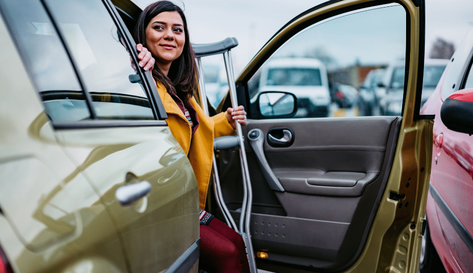 A woman on crutches stepping out of her car.