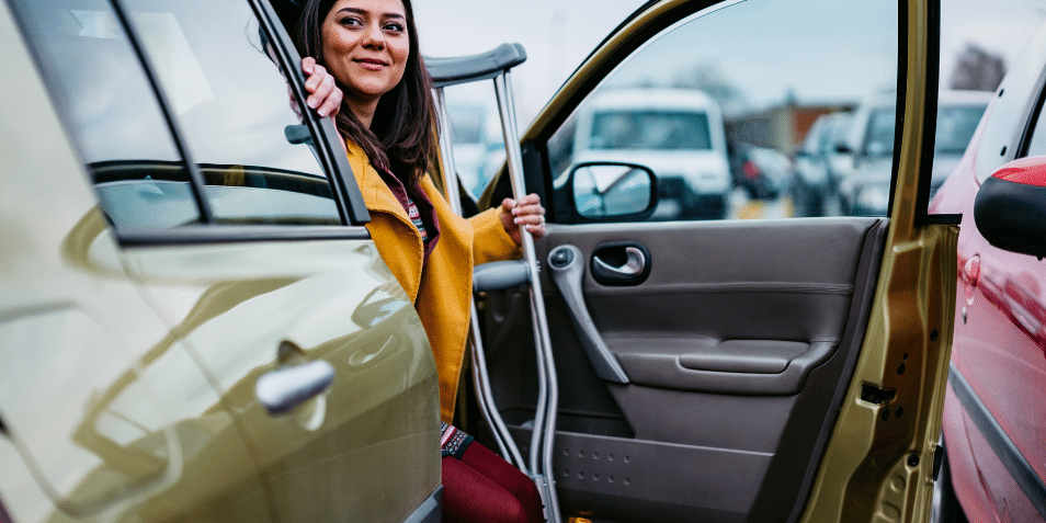 A woman on crutches stepping out of her car.