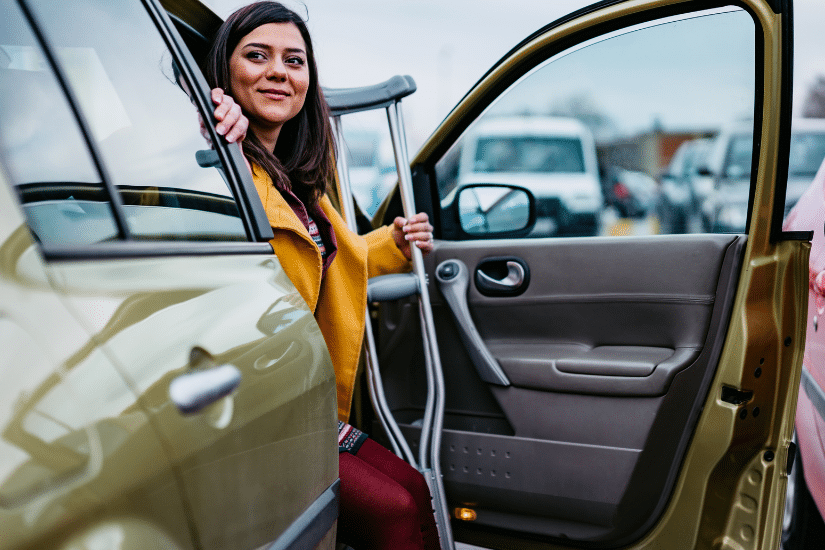 A woman on crutches stepping out of her car.