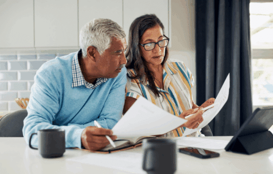 Man and woman sitting at the kitchen table looking at documents.
