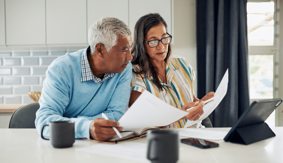 Man and woman sitting at the kitchen table looking at documents.