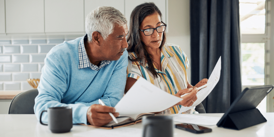Man and woman sitting at the kitchen table looking at documents.