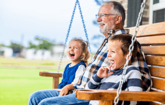 Grandpa sitting on a swing with his grandchildren.