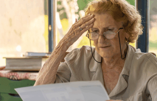 An older woman looking at a piece of paper. She appears stressed.