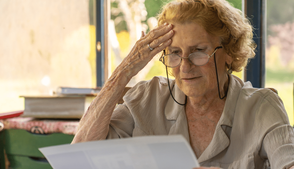 An older woman looking at a piece of paper. She appears stressed.
