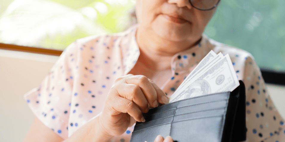 Older woman putting money into her wallet.
