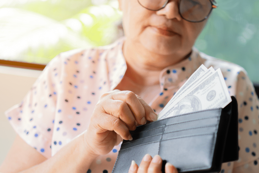 Older woman putting money into her wallet.