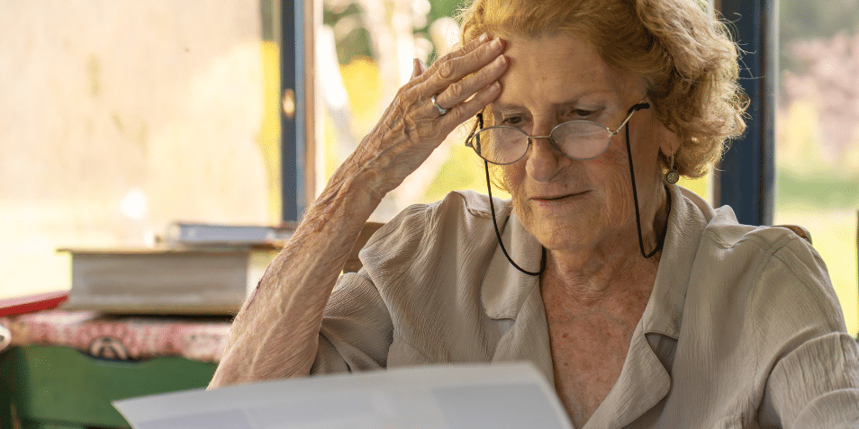 An older woman looking at a piece of paper. She appears stressed.