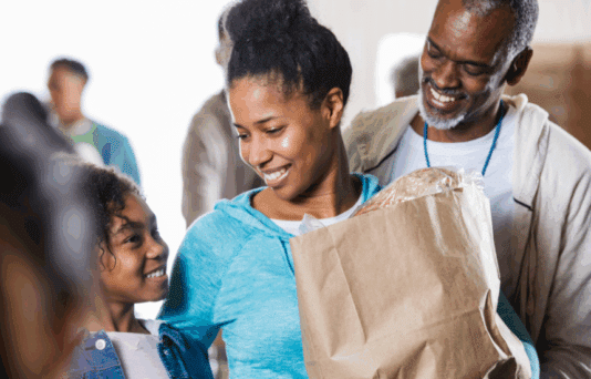 Family smiling, while leaving the grocery store with a bag of food.