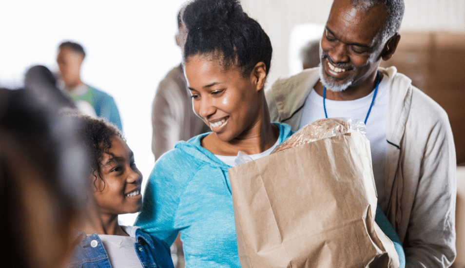 Family smiling, while leaving the grocery store with a bag of food.