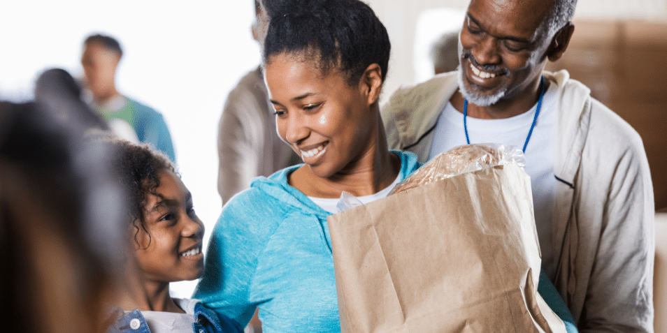 Family smiling, while leaving the grocery store with a bag of food.