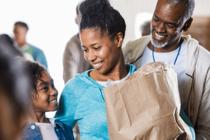 Family smiling, while leaving the grocery store with a bag of food.