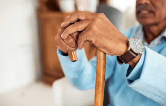 A Black man sitting with his hands on his cane.