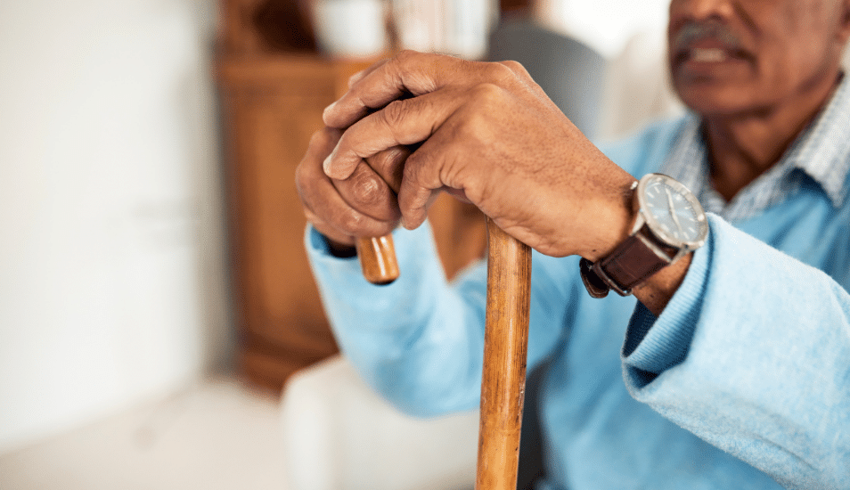 A Black man sitting with his hands on his cane.