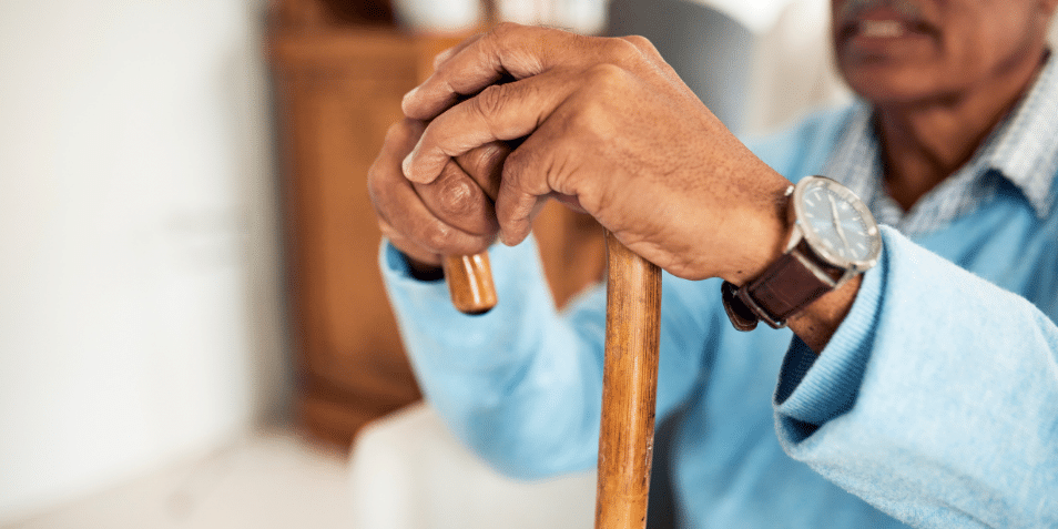 A Black man sitting with his hands on his cane.