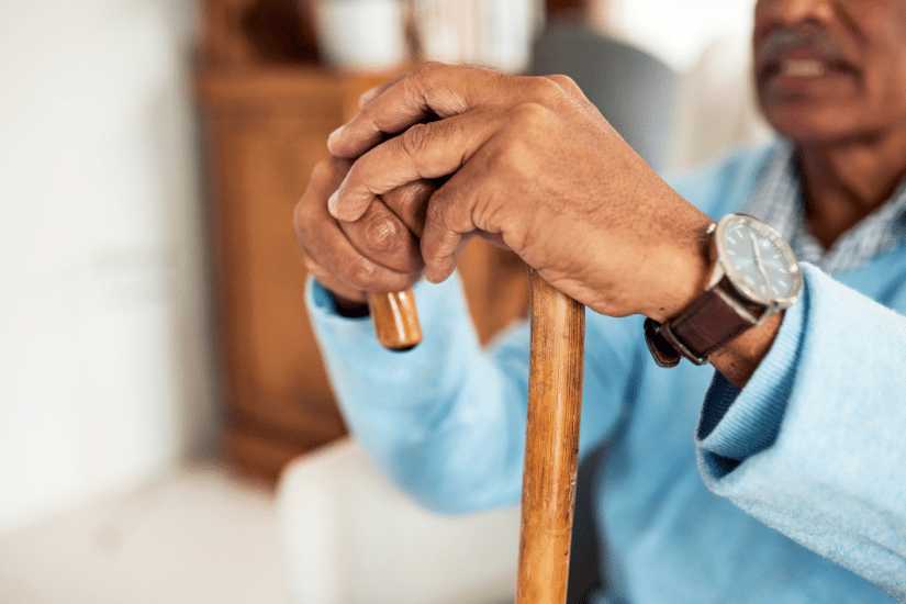 A Black man sitting with his hands on his cane.